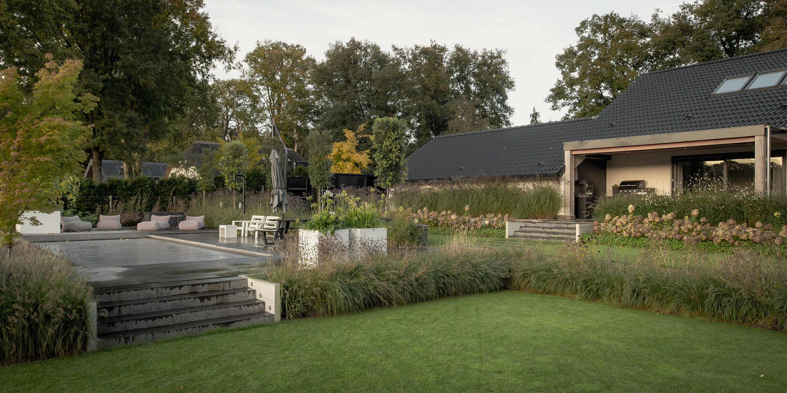 Tuin van Buytengewoon in Hoog Soeren met gazon, traptreden, terras, zwembad en veranda.